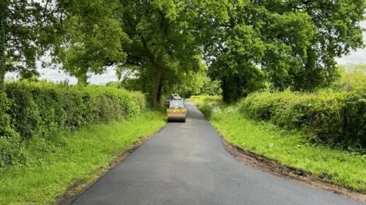 A tarmaced private road being installed with a roller